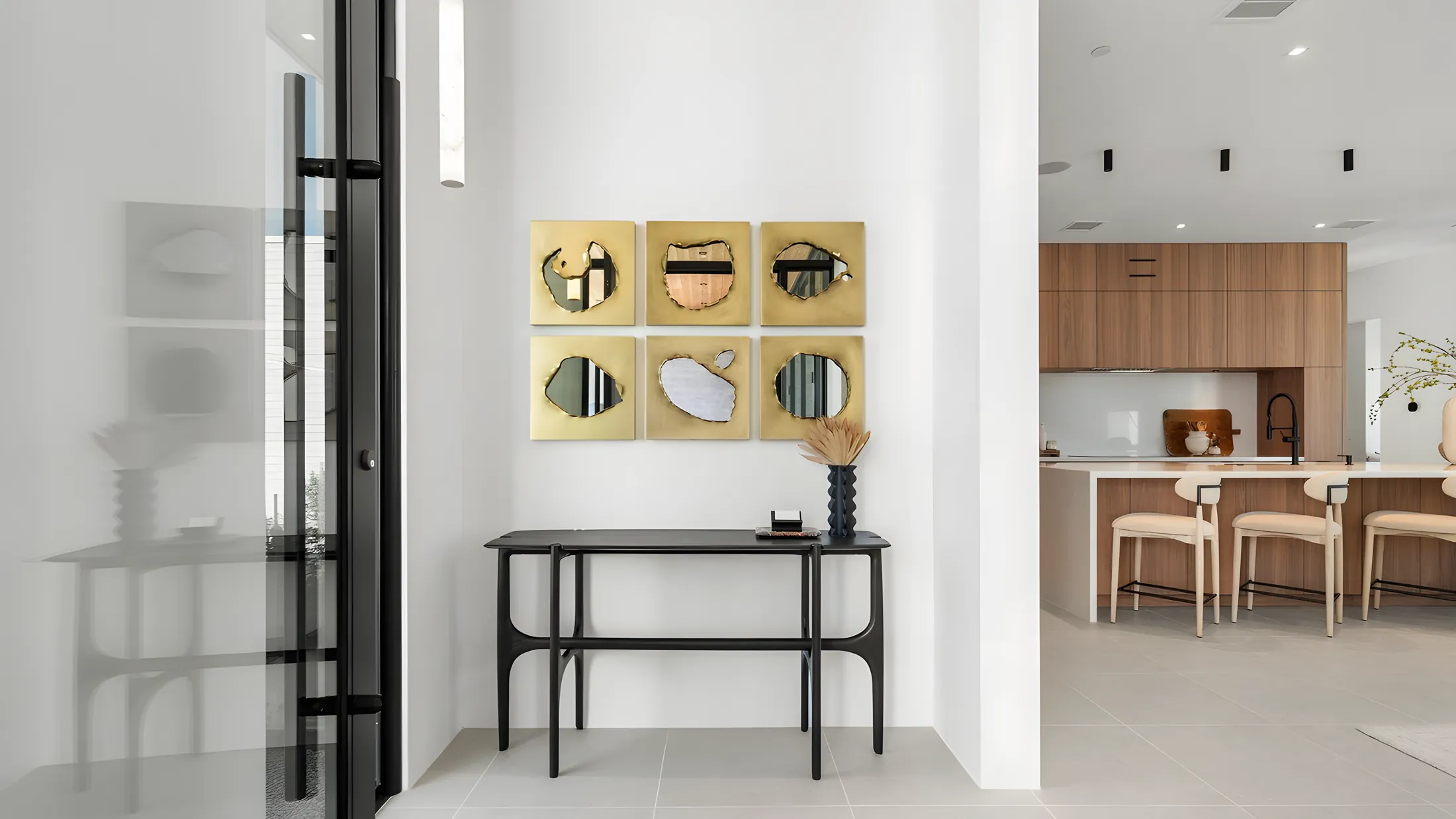 Entry vignette with a sculptural console and brass artwork, opening to the kitchen