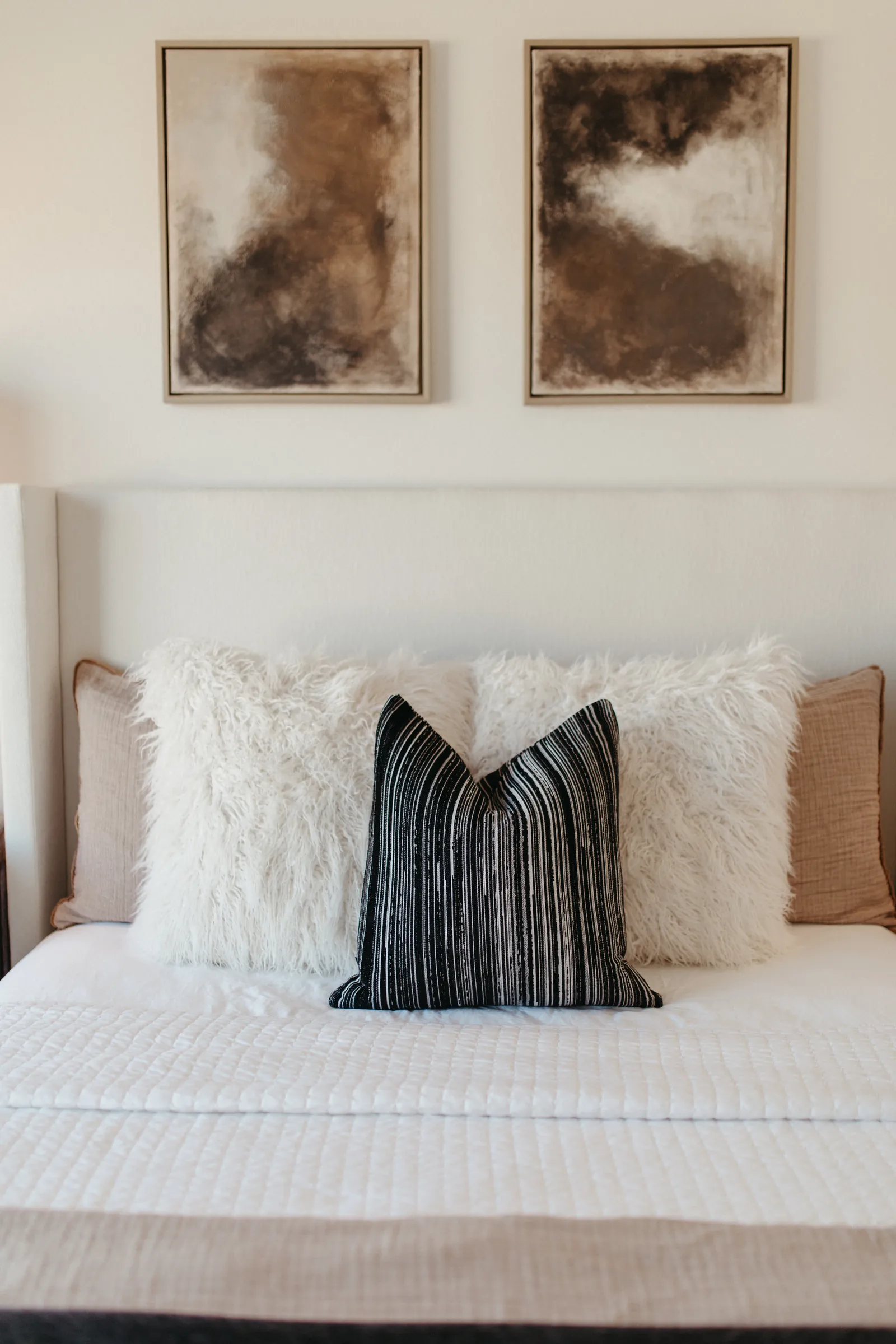 Bedroom with layered neutral bedding and paired artwork